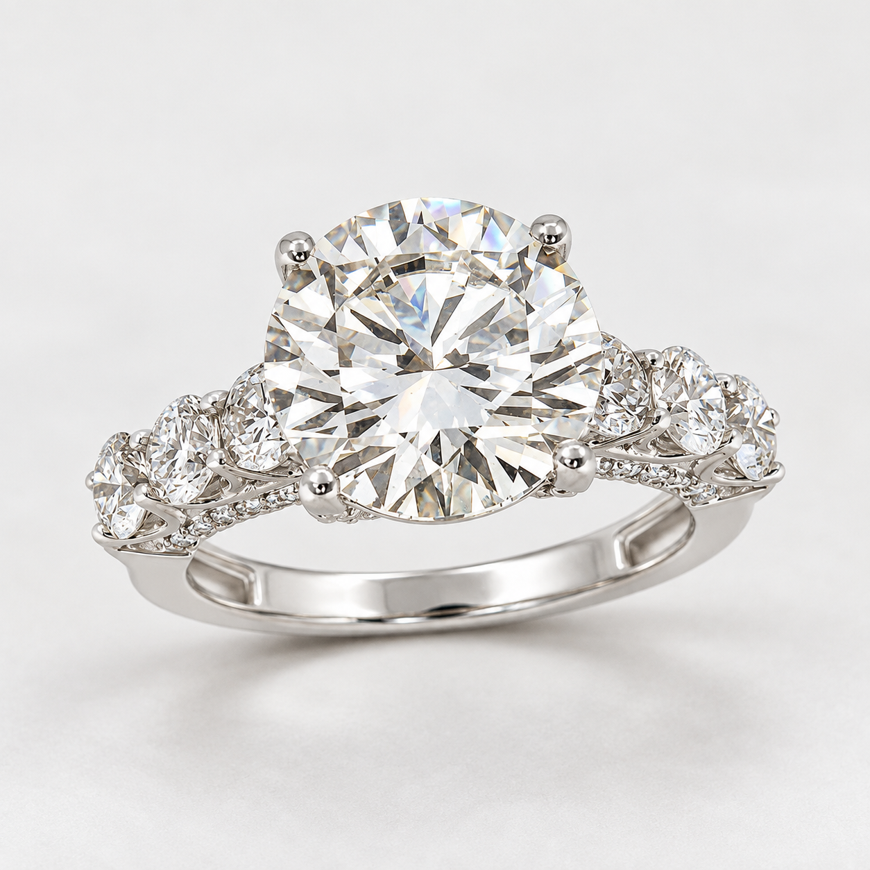 A classic solitaire engagement ring featuring a round brilliant-cut diamond center stone in a four-prong setting, with a split shank adorned with small pavé diamonds, shown on a light gray background.
